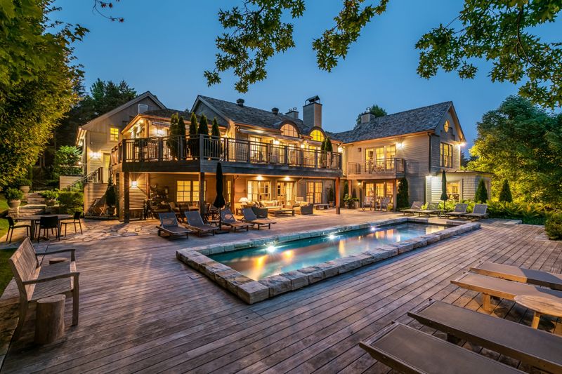 Maison de campagne avec terrasse en bois et piscine illuminée au crépuscule
