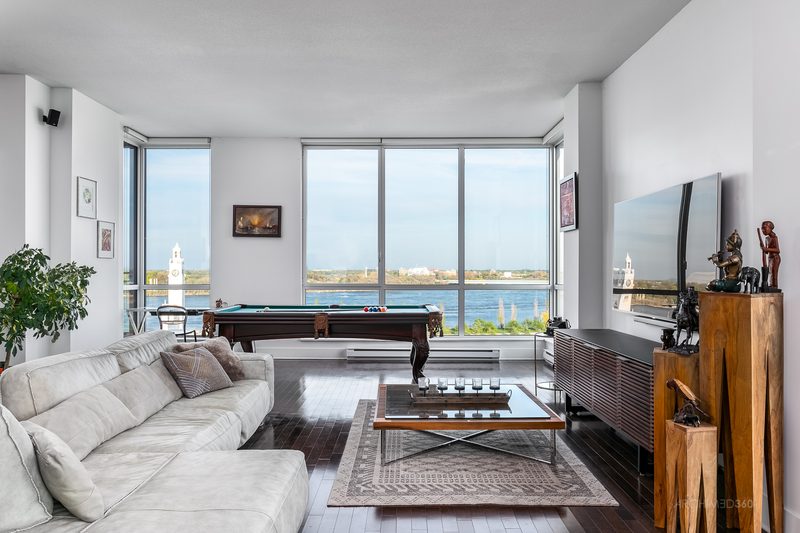Salon d'un condo en hauteur avec de grandes fenêtres donnant sur le fleuve et la Tour de l'Horloge