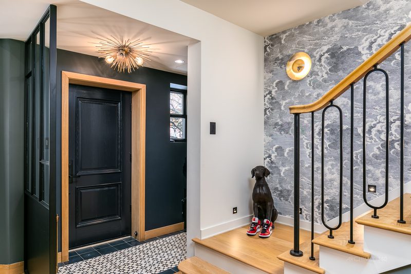 Vestibule avec porte noire, papier peint à motif de nuages et escalier