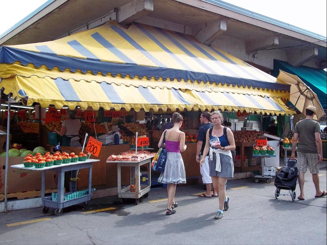 Étal de fruits et légumes sous un auvent jaune et bleu, au marché Jean-Talon