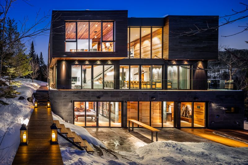Façade vitrée d'une résidence contemporaine illuminée un soir d'hiver, Laurentides