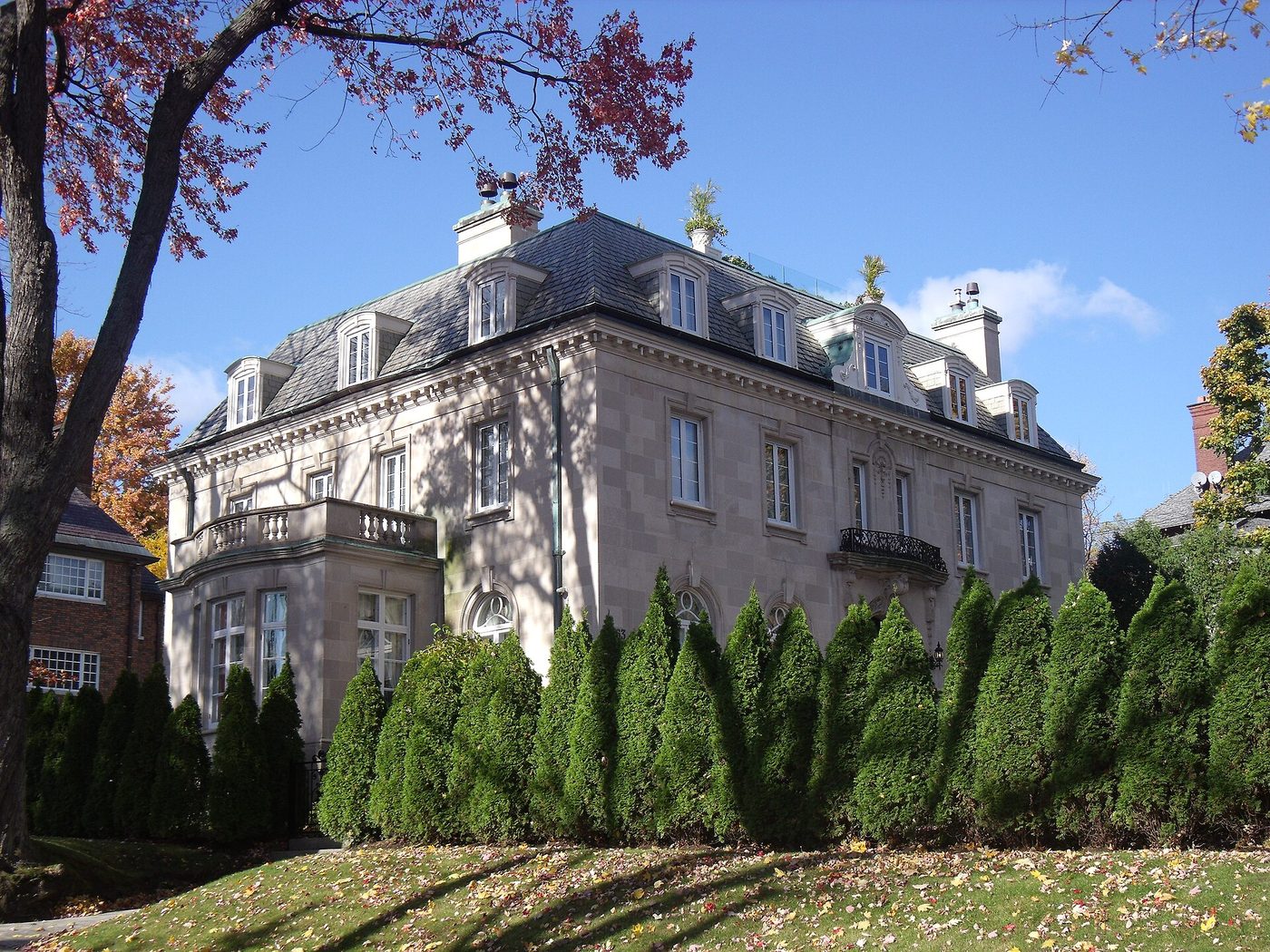 Manoir en pierre de style Beaux-Arts, toit mansardé et haie de cèdres sous les arbres d'automne, Westmount